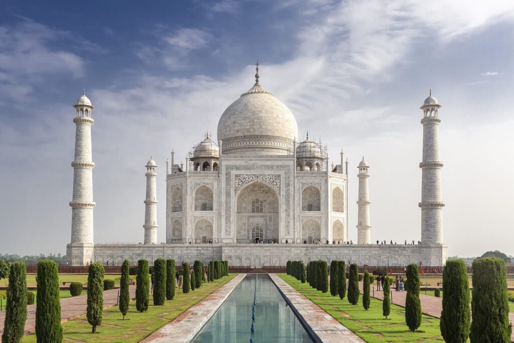 Vista panorámica del Taj Mahal al amanecer, uno de los monumentos más icónicos de la India, con su majestuosa cúpula blanca reflejada en los estanques del jardín.