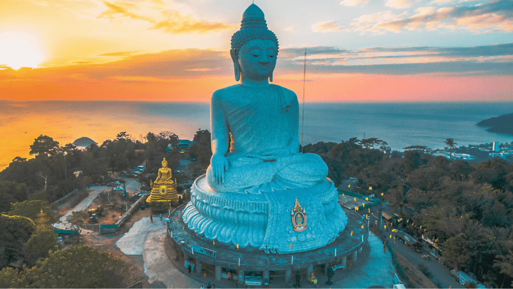 Estatua del Gran Buda de Phuket en primer plano, con vistas al pueblo, el mar y el cielo despejado al fondo