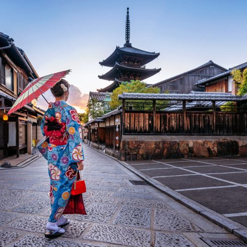 Mujer japonesa con paraguas admirando un templo, una escena típica en los viajes a Japón