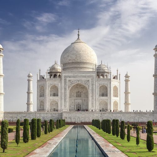 Vista panorámica del Taj Mahal al amanecer, uno de los monumentos más icónicos de la India, con su majestuosa cúpula blanca reflejada en los estanques del jardín.