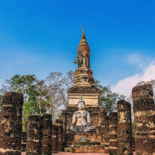 Pasillo que conduce a una estatua de Buda con un monumento histórico al fondo en Sukhothai.