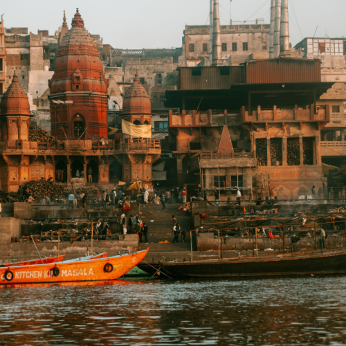 Barquito en el río Ganges con el bullicio de Varanasi al fondo, un destino esencial en los viajes a la India