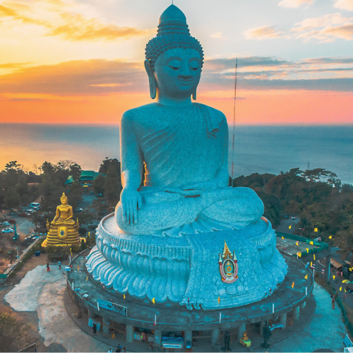 Estatua del Gran Buda de Phuket en primer plano, con vistas al pueblo, el mar y el cielo despejado al fondo