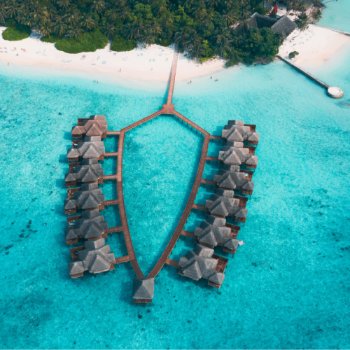 Cabañas sobre el agua cristalina en las Maldivas, rodeadas de un paisaje tropical y cielo despejado.