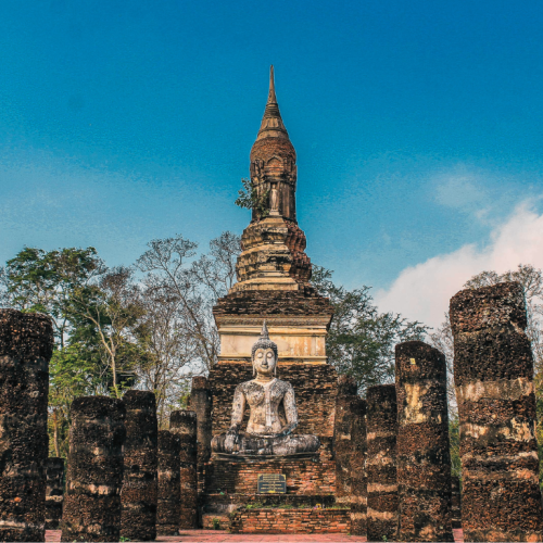 Paseo de piedra en Sukhothai, Tailandia, que conduce a un monumento con un Buda en el centro.